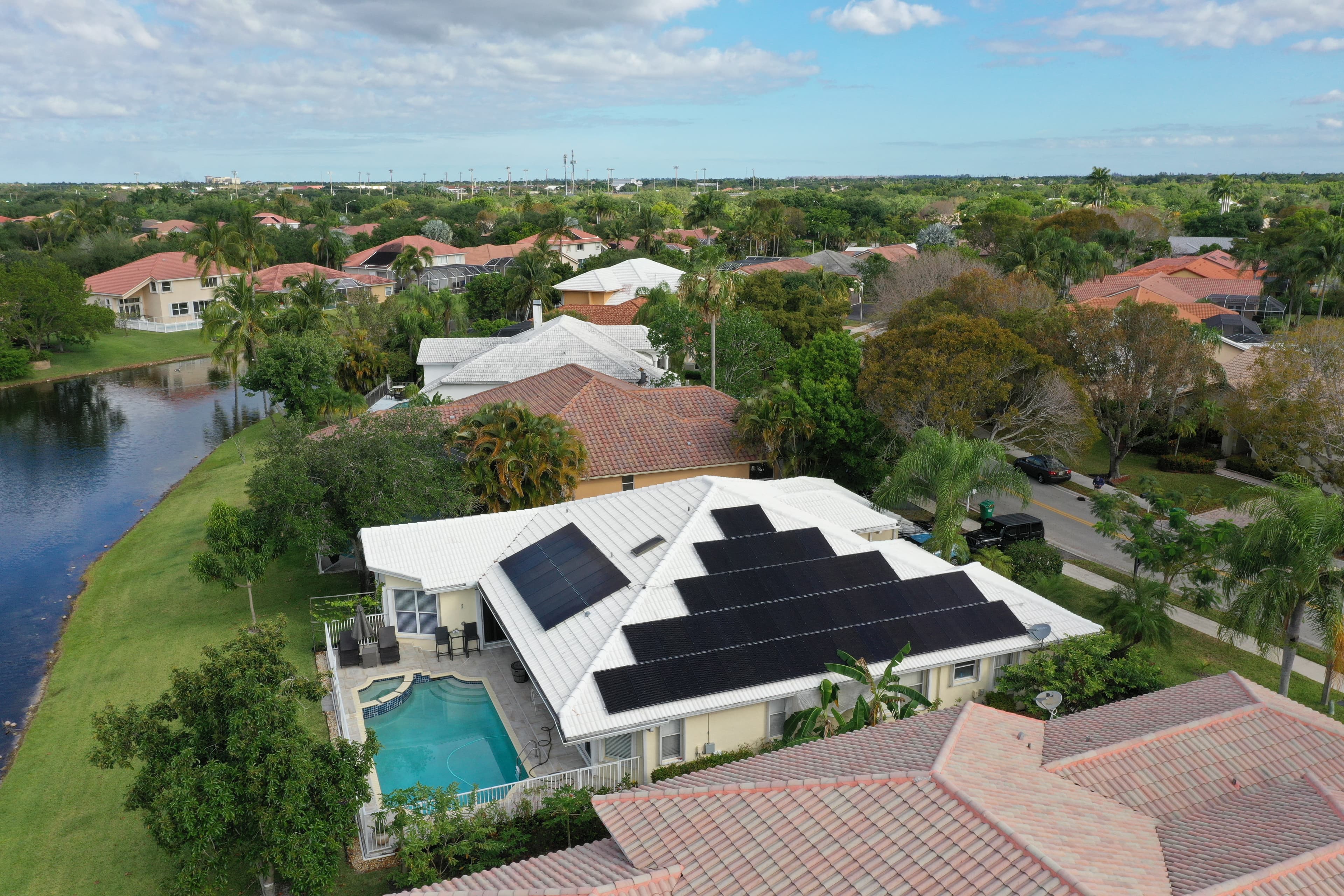 Aerial view of a Florida residential solar array — black panels on a tile roof, pool and lakefront alongside.